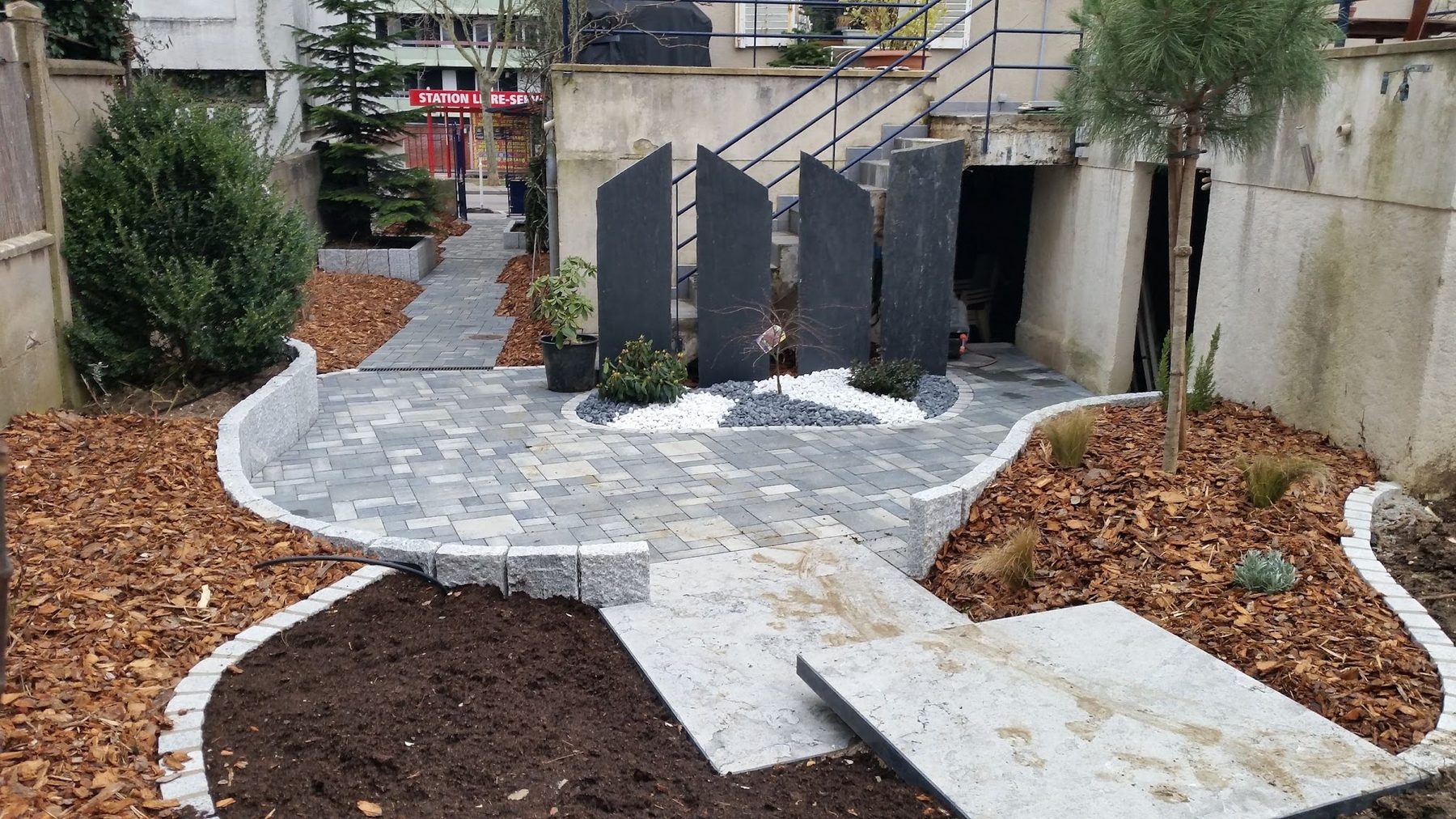 Cour pavée avec bordures en granit, lames d'ardoise et massifs paillés